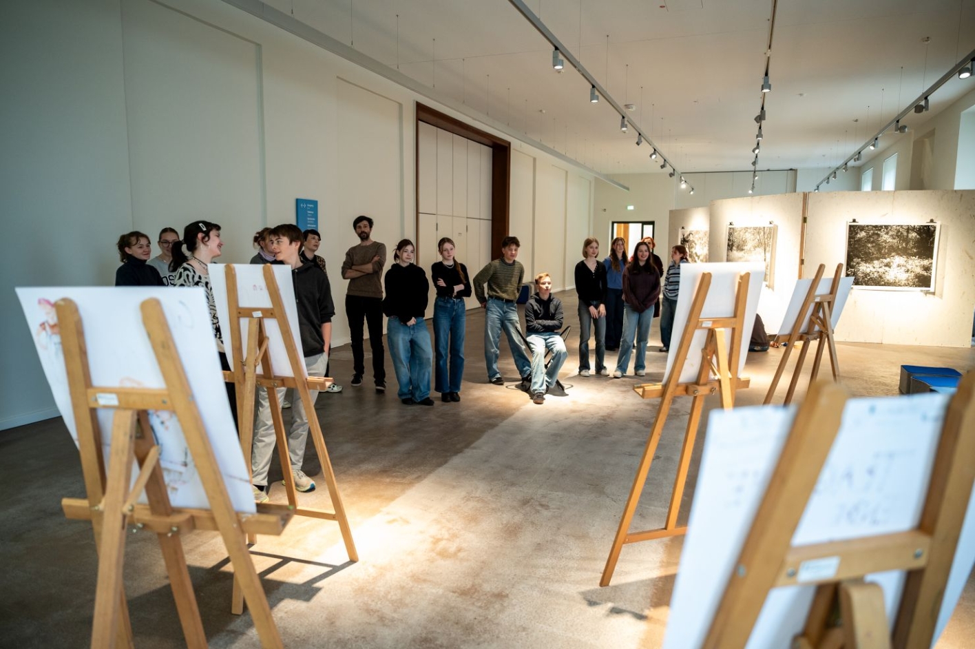 In the foreground are easels with pictures. Many people can be seen in front of the easels.