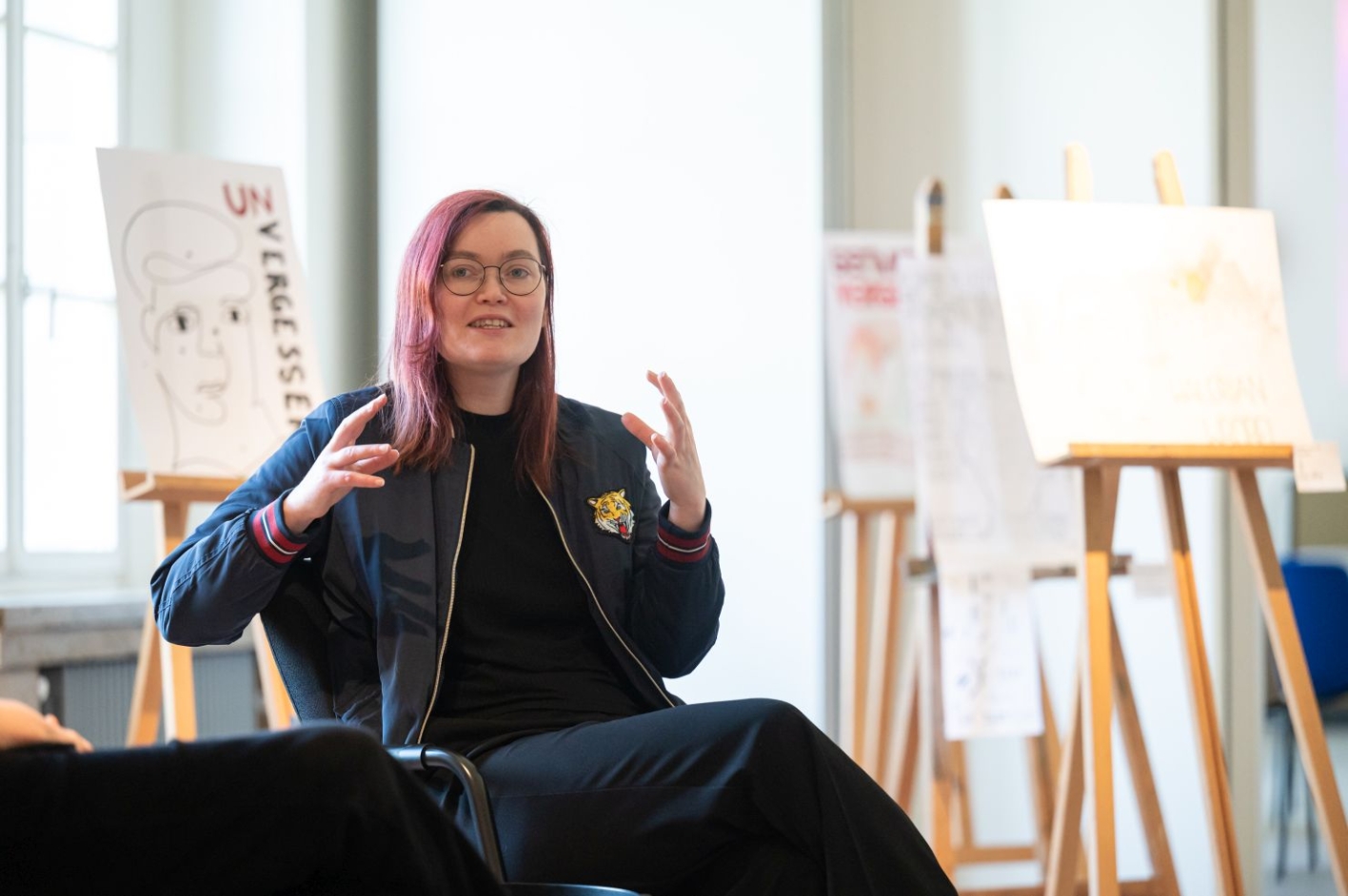 A woman sits on a chair and gesticulates.
