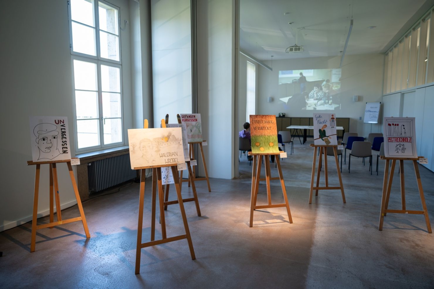 Several easels with posters stand in front of a window.