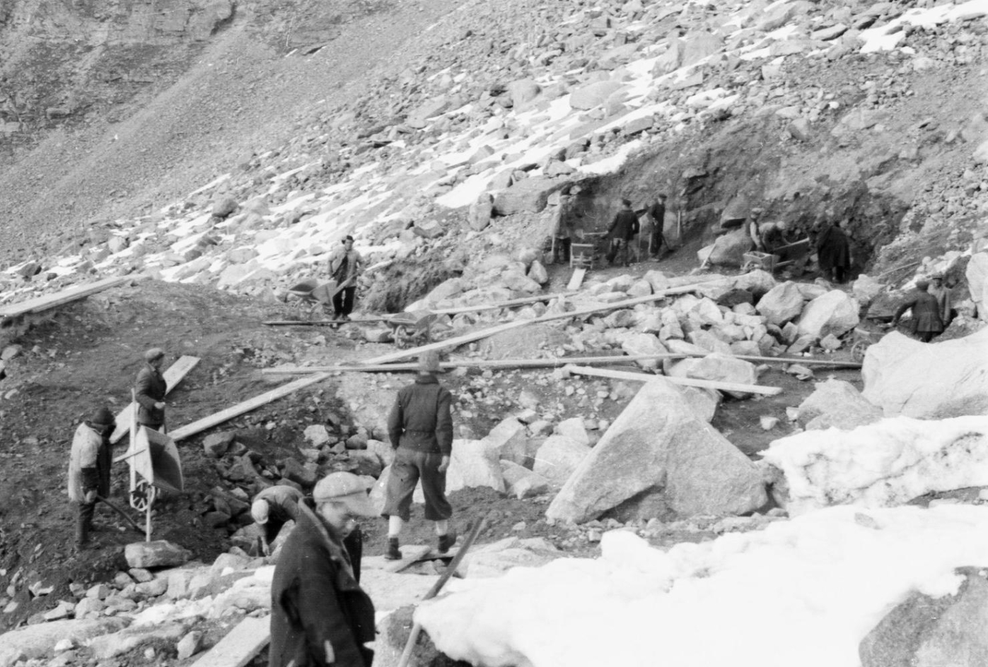 Auf dem Bild sind mehrere Zwangsarbeiter zu sehen, welche im Hochgebirge Steine aus dem Fels schlagen und abtransportieren.