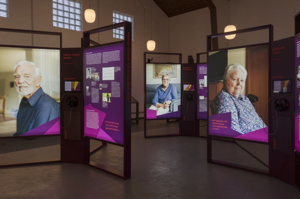 Exhibition view featuring large portrait photographs and informational panels with text