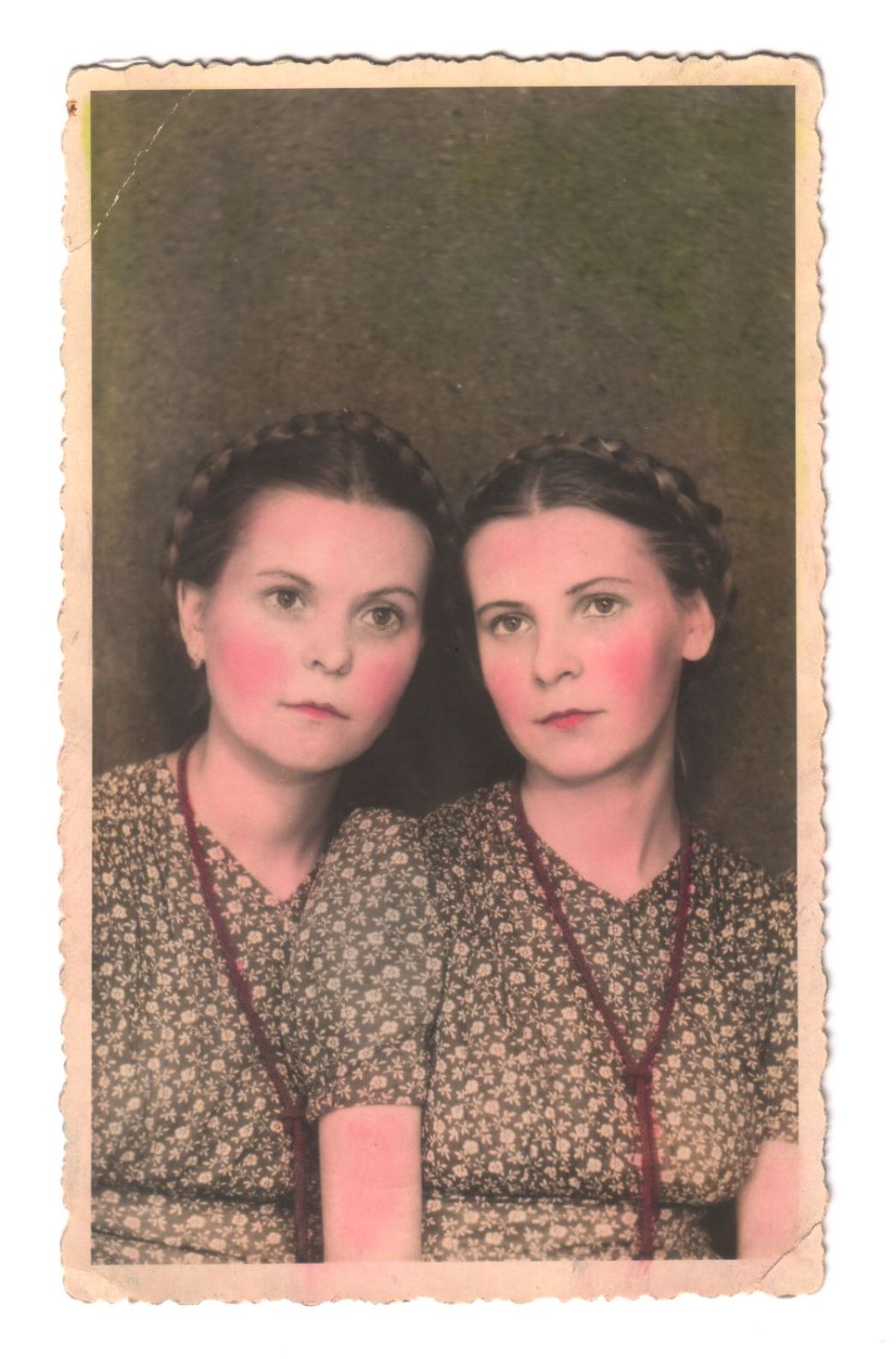 Gabriela Knapska (left) with her twin sister, 1944. The two women look expressionlessly into the camera. They are both wearing make-up and a flowered blouse. The photo is in colour.