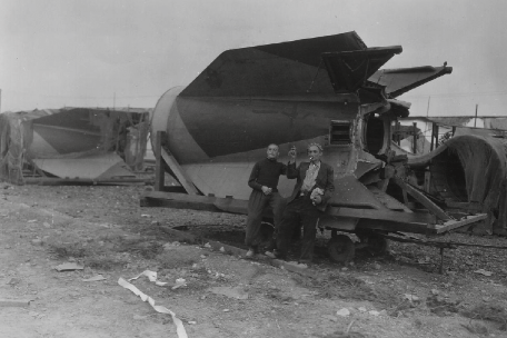 Schwarz-Weiß-Fotografie von zwei befreiten Häftlingen des KZ Mittelbau-Dora vor dem Heck einer V2-Rakete