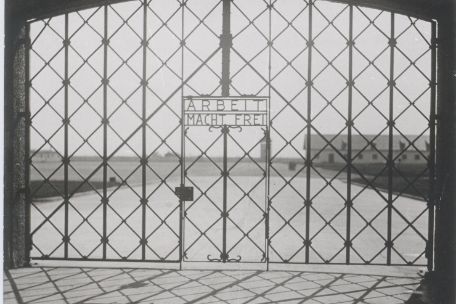 Zu sehen ist ein Eisenes Lagertor. Über der Kleinen Tür in der Mitte steht "Arbeit macht frei" in metallenden Buchstaben.