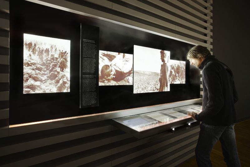 You can see a man looking at the text panels in front of one of the exhibition boxes. Enlarged photographs on the subject of forced labour can be seen in the exhibition boxes.