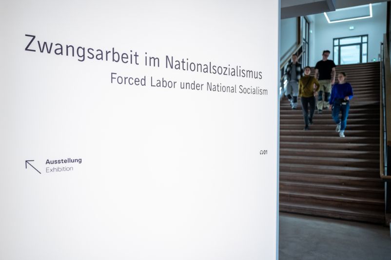 Es ist ein Schriftzug zu erkennnen: "Museum Zwangsarbeit im Nationalsozialismus". Im Hintergrund ist ein Treppenaufgang zu sehen.